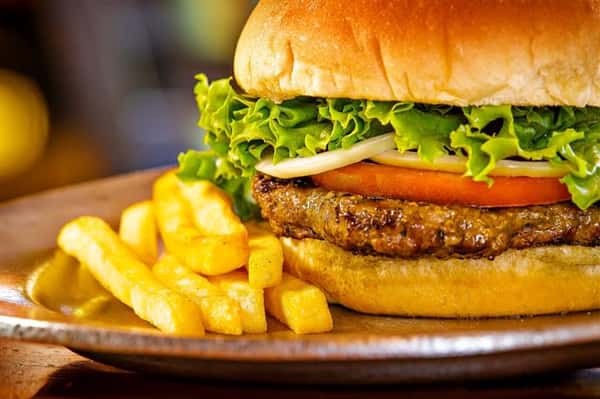 burger on a bun with ham, pineapple slices, tomatoes and lettuce with a side of fries