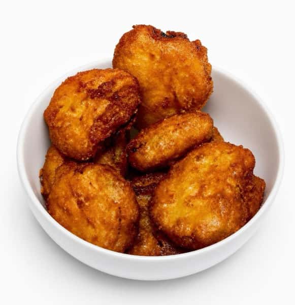 A close-up, top-down view of golden-brown, beer-battered fried pickle chips piled high in a simple white bowl against a stark white background.