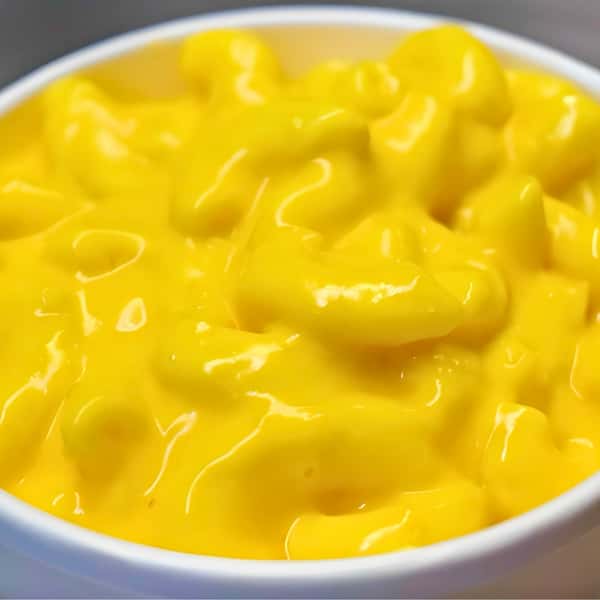 A close-up, mouth-watering view of a white bowl filled with thick, creamy Roasted Garlic Mac and Cheese from Porky's BBQ in Arlington Heights, Illinois, featuring a rich, bright yellow cheese sauce heavily coating the macaroni noodles.