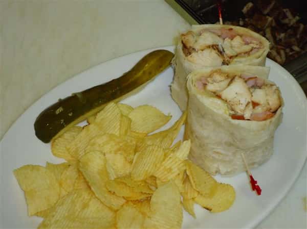 A burrito with a side of chips and a pickle slice