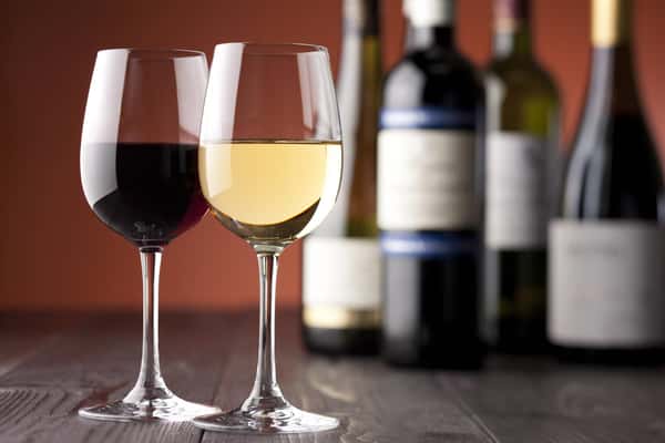 Two half filed glasses of wine in front of four wine bottles