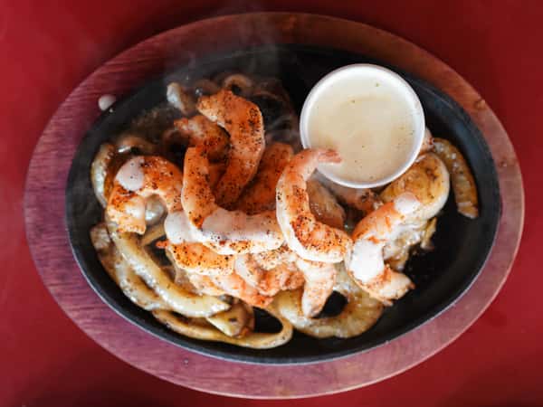 Grilled shrimp served with dipping sauce on a dark platter.