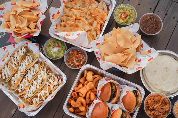 Assorted Mexican dishes including tacos, quesadillas, chips, dips, and sliders arranged on a dining table