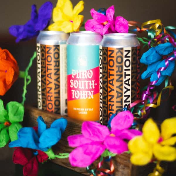 Cans of Puro Southtown Mexican-style lager by Künstler Brewing, surrounded by colorful paper flowers and festive streamers.