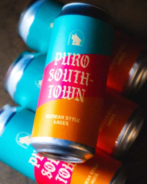 Angled view of Puro Southtown Mexican-style lager cans from Künstler Brewing, featuring bold turquoise, red, and orange branding.