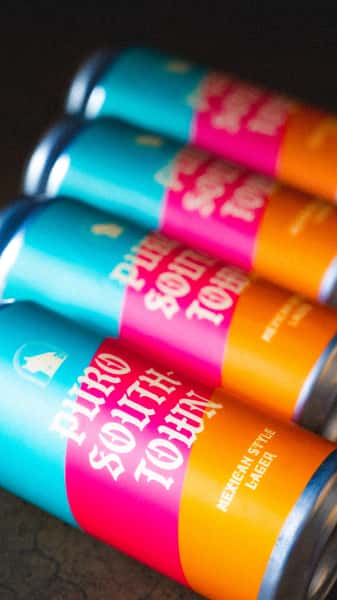 Close-up of multiple Puro Southtown Mexican-style lager cans from Künstler Brewing, featuring bold turquoise, orange, and pink labels.