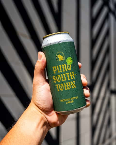 Hand holding a cold Puro Southtown Mexican-style lager can by Künstler Brewing with condensation glistening in the summer sun.