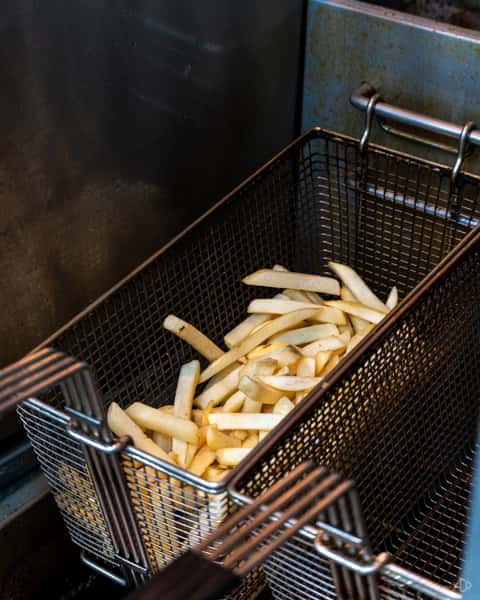 Uncooked French fries in a deep fryer basket, ready to be submerged into hot oil for frying.