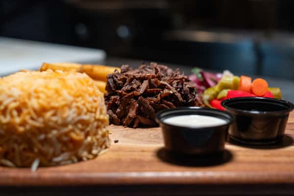 Beef shawarma served with rice, fries, pickled vegetables, and dipping sauces on a wooden platter.
