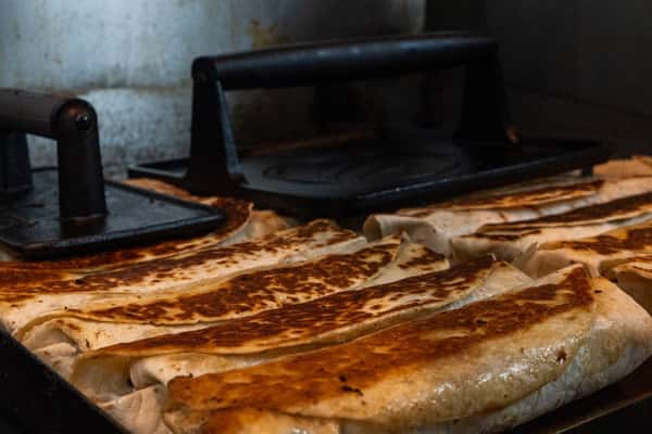 Grilled shawarma wraps being pressed and toasted on a hot flat-top grill using heavy metal grill weights.