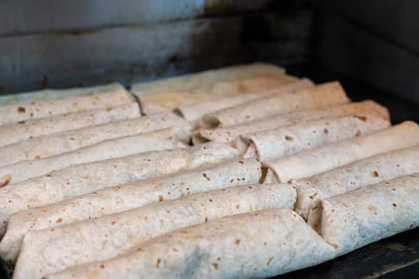 Multiple rolled shawarma wraps arranged closely together on a hot flat-top grill, ready to be toasted or cooked.