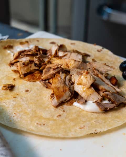 Chicken shawarma slices on a tortilla with a dollop of garlic sauce, ready to be wrapped.