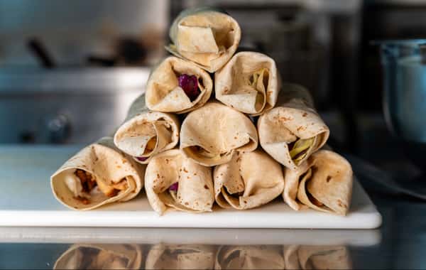 Stacked pyramid of rolled shawarma wraps filled with meat and vegetables, displayed on a white cutting board in a kitchen.
