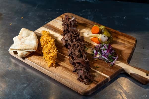 Shawarma platter with sliced beef, Mexican rice, flatbread, pickled vegetables, and red onion salad, arranged on a wooden serving board.