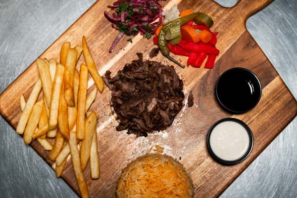 Wooden platter with beef shawarma, fries, rice, pickled vegetables, chopped onions, and two dipping sauces on a metal surface.