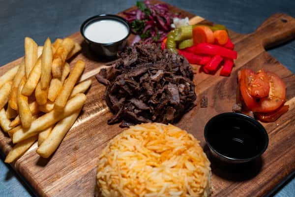 Shawarma platter with beef slices, fries, seasoned rice, pickled vegetables, grilled tomatoes, onions, and two dipping sauces.