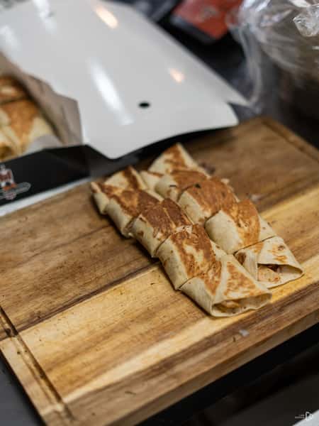 Grilled shawarma wraps sliced into pieces and placed on a wooden cutting board next to a takeout box.