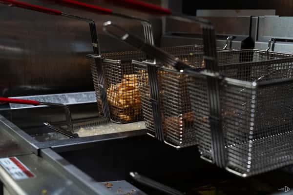 French fries being deep-fried in metal baskets inside a commercial kitchen fryer with bubbling hot oil.