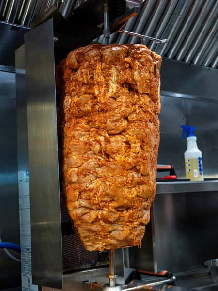 Large vertical rotisserie stacked with marinated raw chicken shawarma meat in a commercial kitchen.