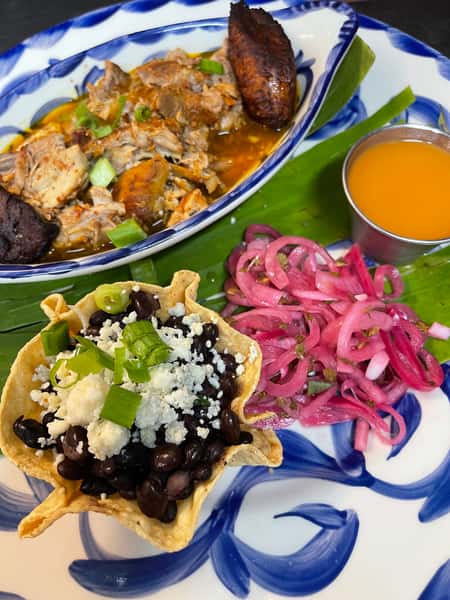 Limited-time Cochinita Pibil at Joselito's Los Angeles, featuring slow-roasted pork, black beans, pickled red onions, and plantains served on a banana leaf.