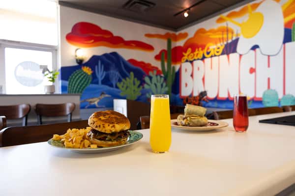 A burger and fries sitting on a table in front of a colorful mountain-themed wall mural.