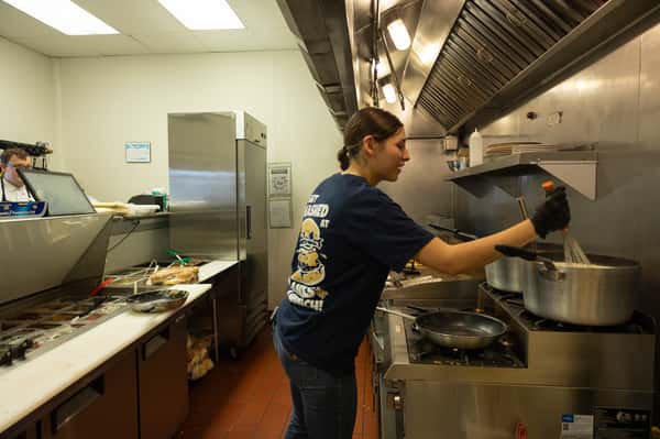 A kitchen staff member working at a stainless steel prep station.
