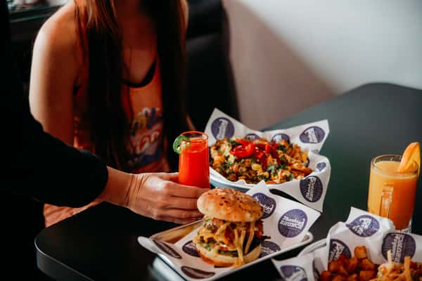A customer at a table with a burger and a red cocktail.