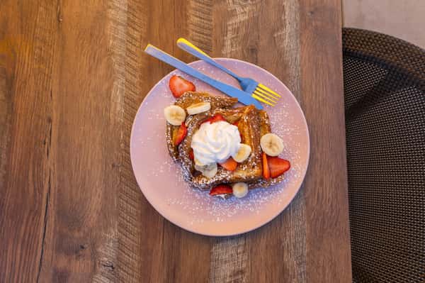 An overhead view of French toast topped with strawberries, bananas, and whipped cream.