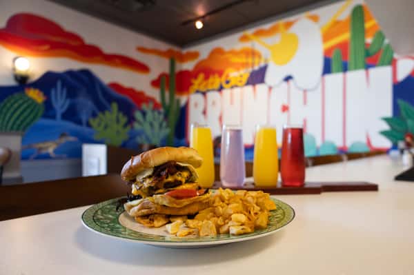 A burger plate accompanied by three colorful juice drinks.