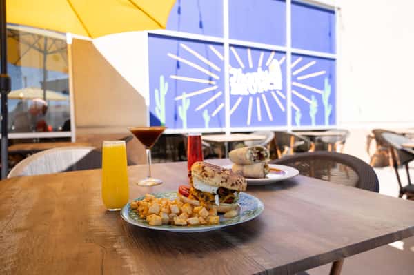A table set with orange juice glasses and plates against a mural background.
