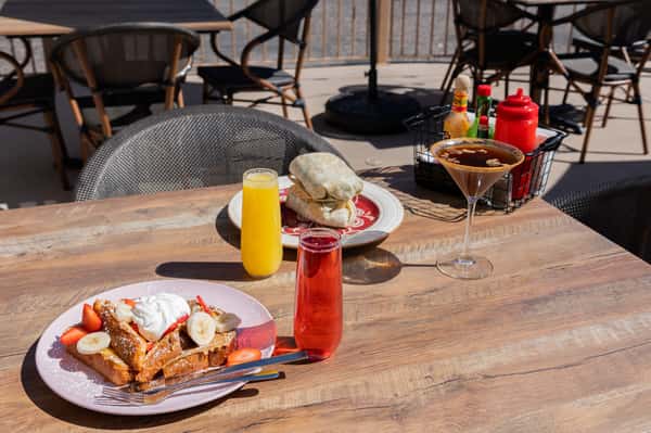 A close-up of brunch dishes and drinks on an outdoor table in the sun.
