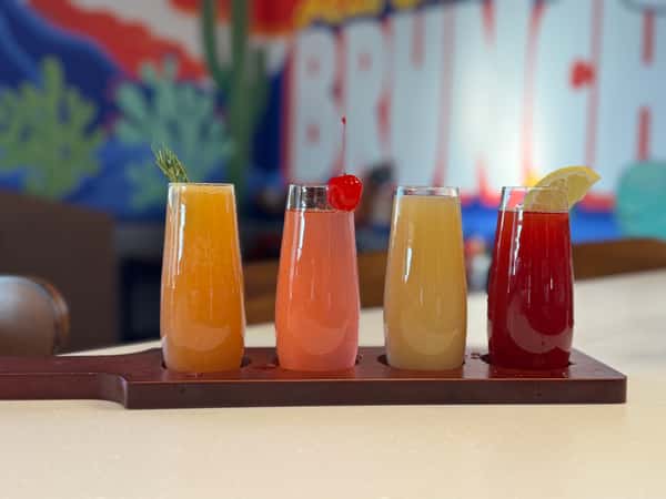 flight of four different colored mimosas or juices on a wooden board.