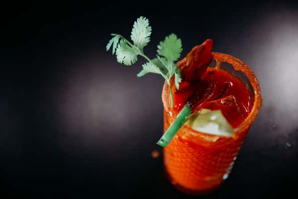 A close-up of a red cocktail in a jar glass with a salted rim and garnish.