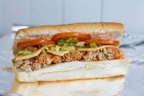 A steak and cheese sub with tomatoes, lettuce, and cheese is displayed at Steak N' Cheese Please.