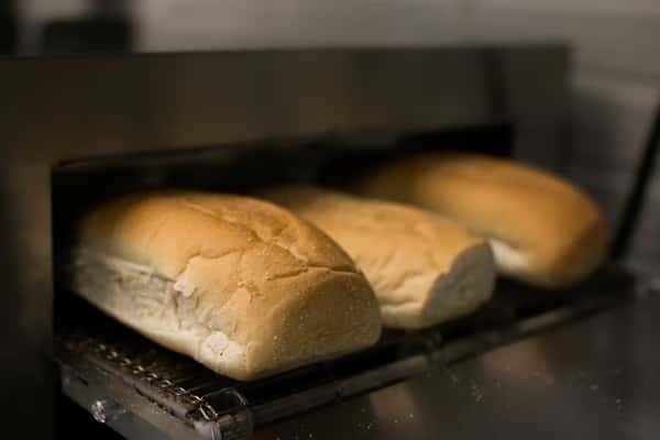 Submarine sandwich rolls are being toasted in a conveyor toaster at Steak N' Cheese Please.