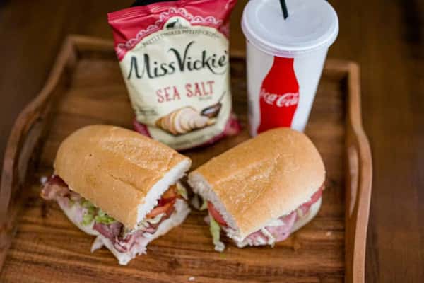 A Steak N' Cheese Please sub sandwich, Miss Vickie's chips, and a Coca-Cola on a wooden tray.