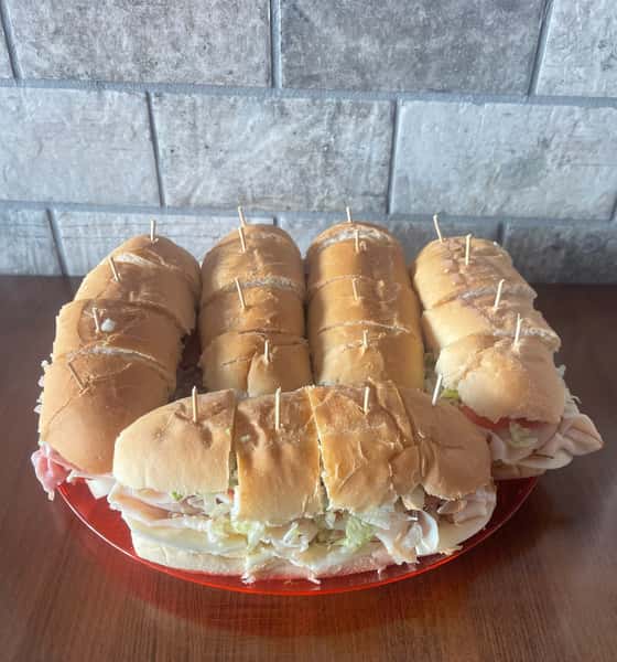 Several cut submarine sandwiches with toothpicks are arranged on a red plate at Steak N' Cheese Please.