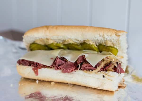 A fully loaded sandwich with meat, cheese, and pickles, possibly a specialty at Steak N' Cheese Please.