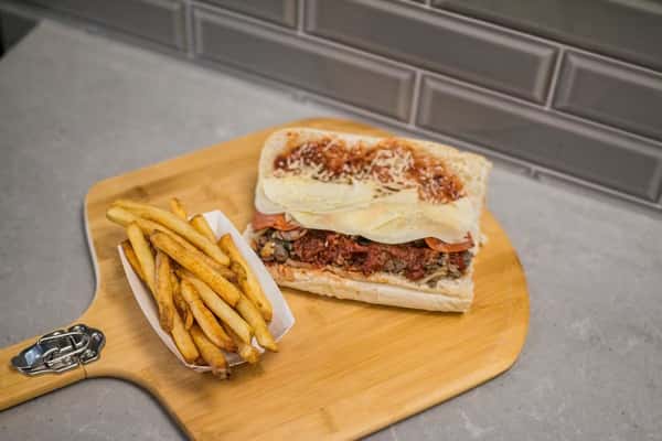 A steak and cheese sub with fries is presented on a wooden board at Steak N' Cheese Please.