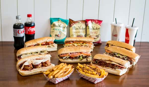 Variety of sandwiches, fries, chips, and drinks arranged on a table at Steak N' Cheese Please.