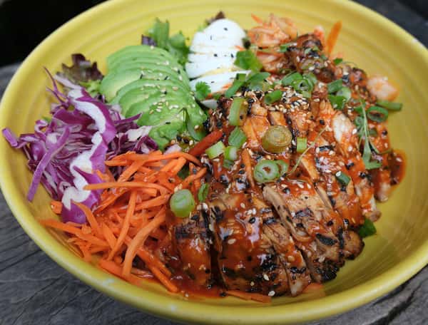 Korean-inspired rice bowl with grilled chicken, spicy sauce, avocado, cabbage, carrots, scallions, and sliced boiled egg.