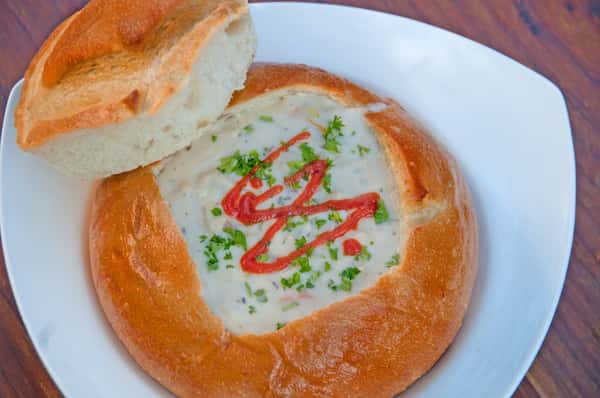 Creamy soup served in a toasted bread bowl, topped with chopped parsley and a swirl of sriracha for a spicy kick.