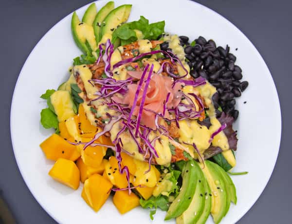 Tropical salad with grilled fish, avocado, mango, black beans, and shredded cabbage, drizzled with creamy dressing and pickled ginger.