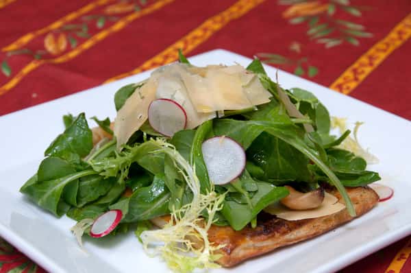 Fresh spinach and arugula salad with radish slices, shaved parmesan, and mushrooms over a golden puff pastry base.