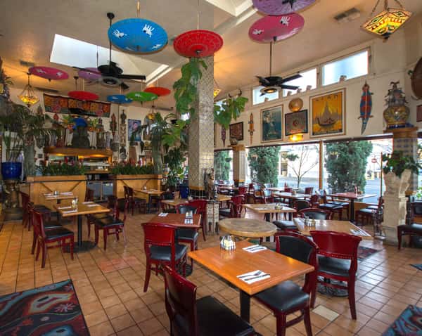 Eclectic dining room with global décor, vibrant parasols on the ceiling, mosaic columns, and large windows bringing in natural light.