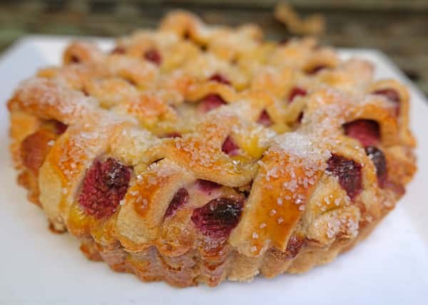 Golden lattice berry tart with sugared crust and juicy raspberries baked into a flaky pastry, served on a white plate.