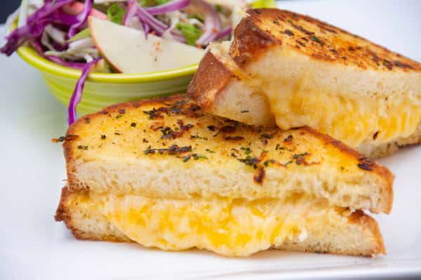 Golden grilled cheese sandwich with melted cheddar on herb-crusted bread, served with a crisp apple and cabbage slaw.