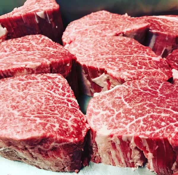 Several thick cuts of raw dark red meat with intricate white marbling.