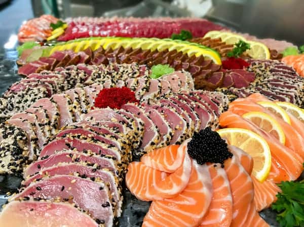 A platter of various seafood sashimi, including sesame-crusted tuna, salmon with lemon slices and black caviar, and red caviar.