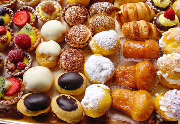 Assorted pastries including fruit tarts, cream puffs, mini croissants, and rum babas.